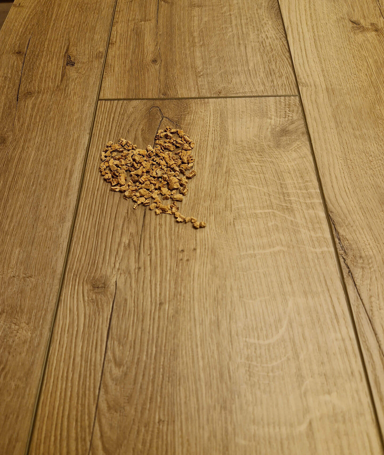 Vinylboden in Holzoptik mit einem herzförmig ausgelegten Dekor aus Holzspänen.