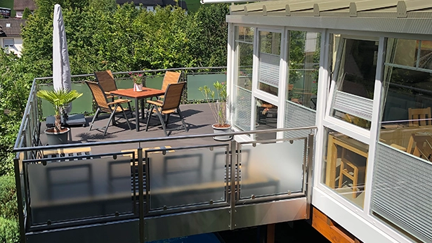 Dachterrasse mit Sitzgruppe, Glasgeländer und angrenzendem Wintergarten.