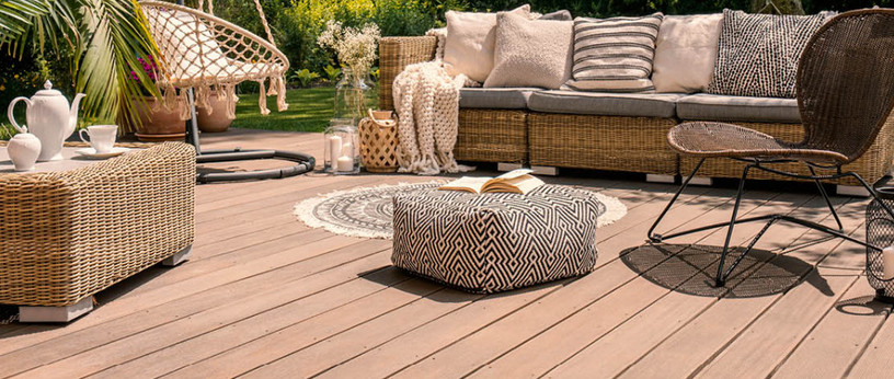 Gemütliche Terrasse mit Holz- oder WPC-Dielen, stilvollen Rattanmöbeln, Hängesessel, dekorativen Kissen und stimmungsvoller Gartengestaltung.