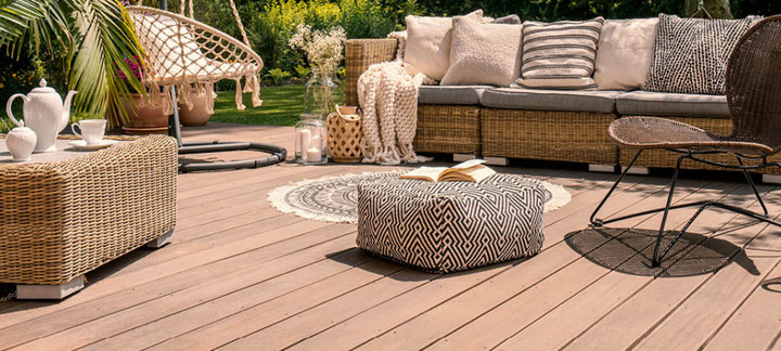 Gemütliche Terrasse mit Holz- oder WPC-Dielen, stilvollen Rattanmöbeln, Hängesessel, dekorativen Kissen und stimmungsvoller Gartengestaltung.