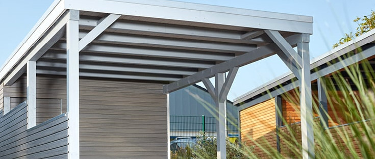 Carport mit Holzdach als Unterstand für ein geparktes Auto.