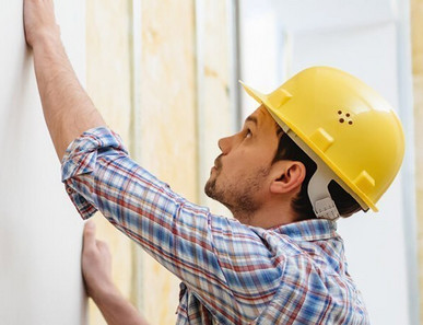 Handwerker mit gelbem Schutzhelm montiert eine Gipskartonplatte auf eine Metallständerwand mit Dämmung.