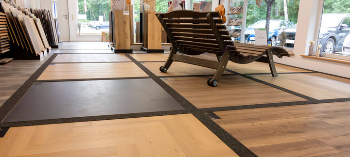 Showroom mit verschiedenen Bodenbelag-Mustern in Holz- und Fliesenoptik, im Vordergrund eine Gartenliege aus Holz.