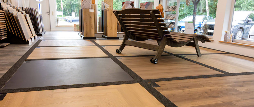 Showroom mit verschiedenen Bodenbelag-Mustern in Holz- und Fliesenoptik, im Vordergrund eine Gartenliege aus Holz.