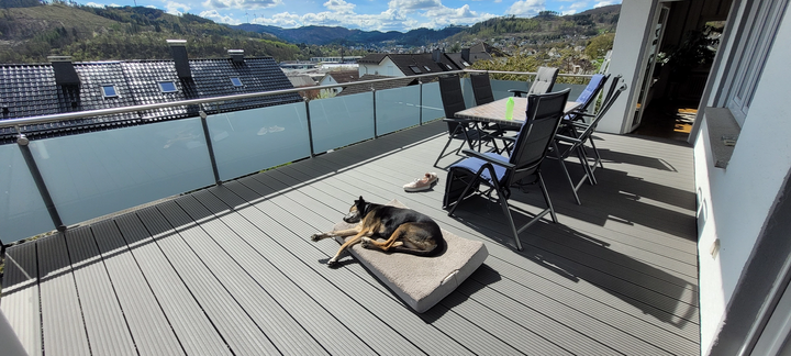 Geräumige Dachterrasse mit WPC-Dielenboden, Glasgeländer, Sitzgruppe und Panoramablick über das Tal.