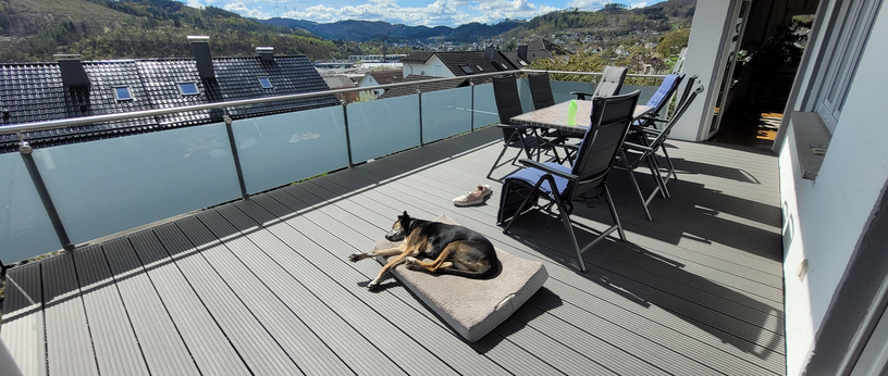 Geräumige Dachterrasse mit WPC-Dielenboden, Glasgeländer, Sitzgruppe und Panoramablick über das Tal.